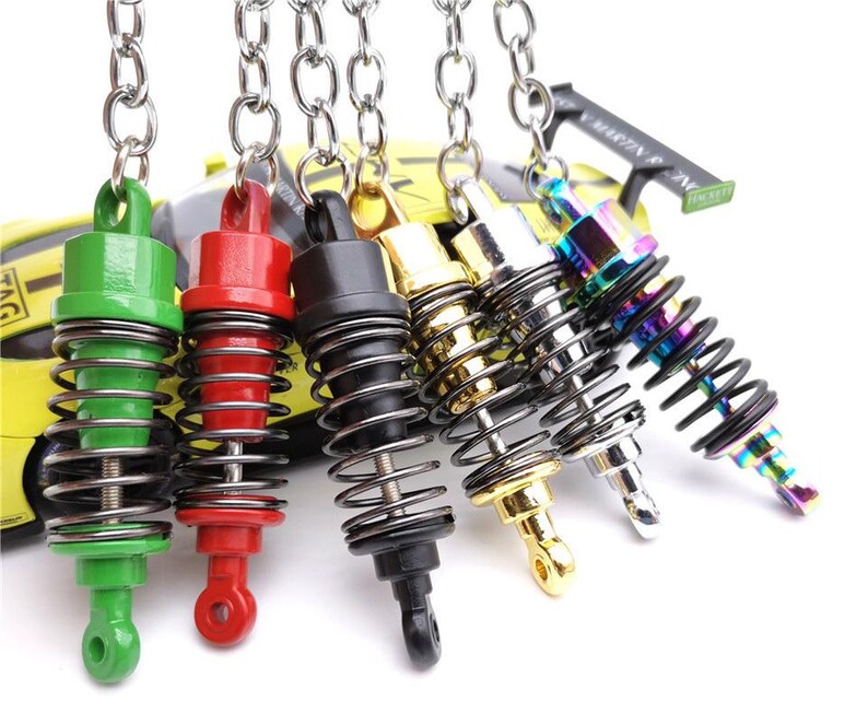 May include: A collection of colorful miniature shock absorber keychains. The keychains feature a variety of colors, including green, red, black, gold, silver, and iridescent. Each keychain has a metal spring and a chain for attaching to keys.