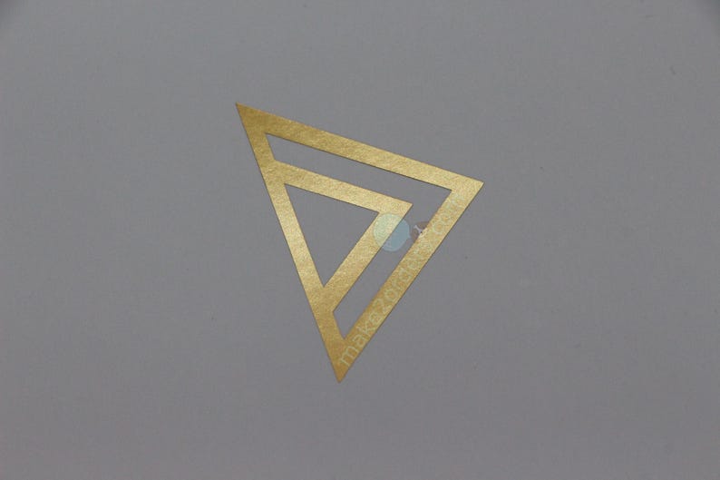 May include: A gold-coloured geometric design, featuring a layered triangle shape, is centred on a grey background. The text "makezotik" is visible on the design. The overall aesthetic is minimalist and modern.