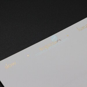 May include: A white and gold business card with the words "slow" and "luxury" printed in gold. The card is on a black surface. The website address is also visible.