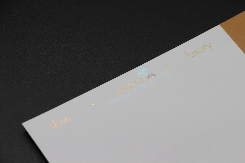May include: A white and gold business card with the words "slow" and "luxury" printed in gold. The card is on a black surface. The website address is also visible.