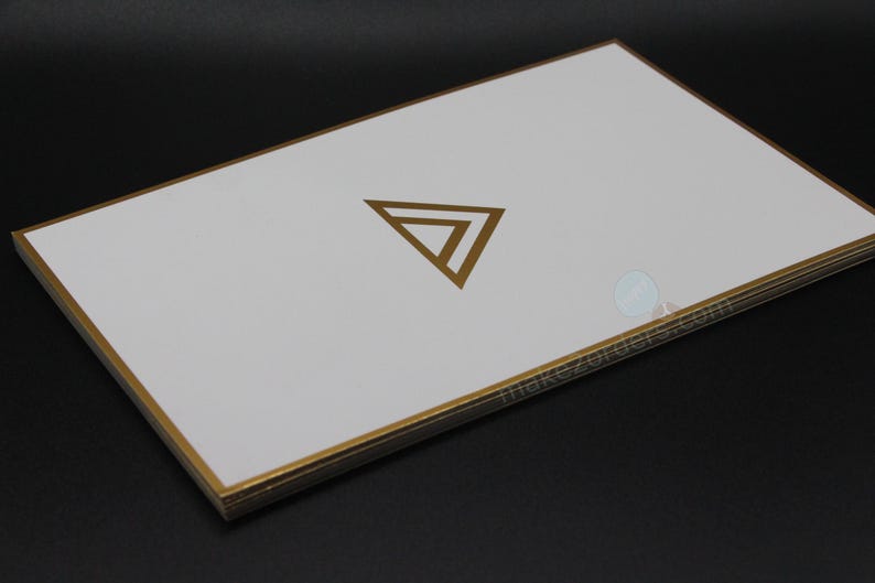 May include: A stack of white cards with gold edges and a gold geometric logo. The cards are rectangular and have a clean, minimalist design. The gold accents provide a touch of elegance. The cards are likely used for business or promotional purposes.