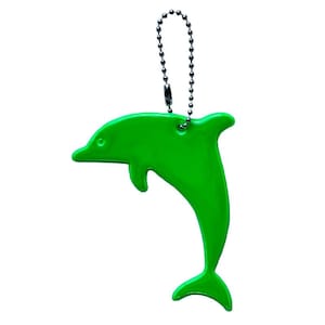Puede incluir: Un llavero con forma de delfín de color verde brillante. El dije está hecho de un material brillante y está unido a una cadena de bolas plateada. El delfín tiene un diseño suave y curvado.