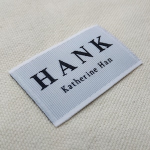 May include: A rectangular label with the name "HANK" in bold black letters and "Katherine Han" in smaller black letters. The label is light gray with a textured pattern and white borders.