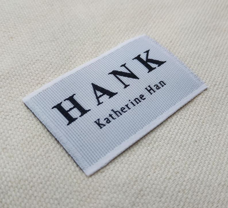 May include: A rectangular label with the name "HANK" in bold black letters and "Katherine Han" in smaller black letters. The label is light gray with a textured pattern and white borders.