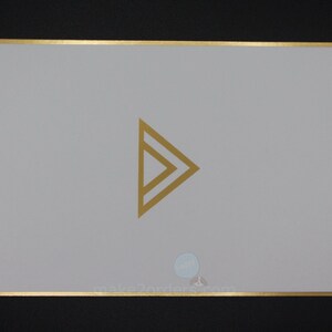 May include: A rectangular card with a gold border and a gold geometric arrow design in the centre. The card is light grey, and the background is black. The website address make2orders.com is at the bottom.