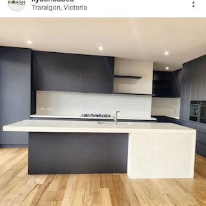 May include: A modern kitchen with dark gray cabinets, white countertops, and a large island. The island has a white countertop and a dark gray base. The floor is made of light wood.