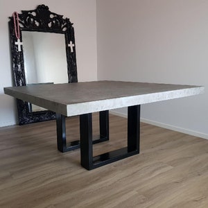 May include: A rectangular concrete table with a grey top and black metal legs. The table is sitting on a wooden floor.