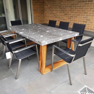May include: A large rectangular table with a grey concrete top and wooden legs. The table is surrounded by six black chairs with stainless steel frames.