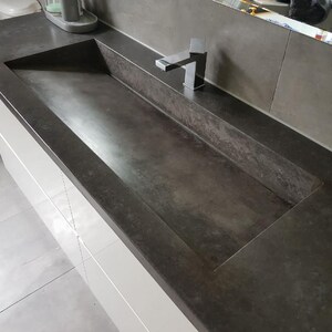 May include: A rectangular dark gray concrete bathroom sink integrated into a matching countertop. The basin features a flat, sloped bottom and straight edges. A polished chrome single-handle faucet is mounted on the rear deck of the sink.