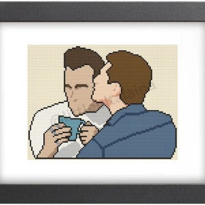 May include: Two men are shown in a cross-stitch pattern. The man on the left is wearing a white shirt and holding a blue mug. The man on the right is wearing a blue shirt and is leaning in to kiss the man on the left.