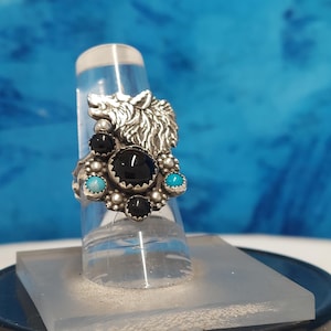 May include: A silver ring with a wolf head design and black and turquoise stones.