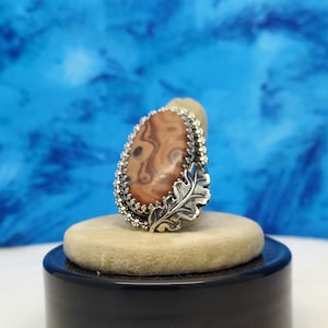 May include: A silver ring with a brown and white agate stone set in a silver leaf design.