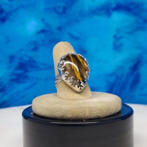 May include: A silver ring with a teardrop-shaped brown and yellow gemstone set in a silver filigree design.