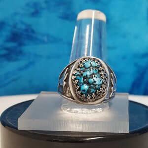 May include: A silver ring with a turquoise stone set in a detailed design. The stone is a mottled blue and green color.