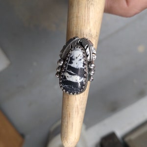 Ladies Ring is a size 6 1/2 and has a 14 x 25 mm White Buffalo Turquoise in a gallery bezel, with 2  feathers and balls and a detailed band.