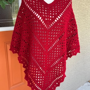 May include: A vibrant red, open-weave crochet poncho with a V-neck. The poncho features a chevron design and a scalloped edge. This handmade garment is displayed on a mannequin.