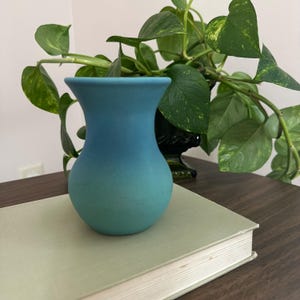 May include: A small, matte-finish vase featuring a smooth gradient color transition from a deep sky blue at the flared rim down to a lighter, vibrant turquoise at the rounded base, creating a clean and simple aesthetic for this ceramic vessel.