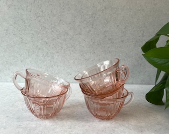 Puede incluir: Conjunto de cuatro tazas de té de vidrio rosa con un diseño acanalado. Las tazas están apiladas una encima de la otra, con la taza superior con asa.