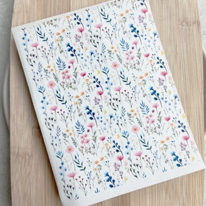 May include: A white sheet of paper with a repeating pattern of pink, blue, and yellow wildflowers on a white background.