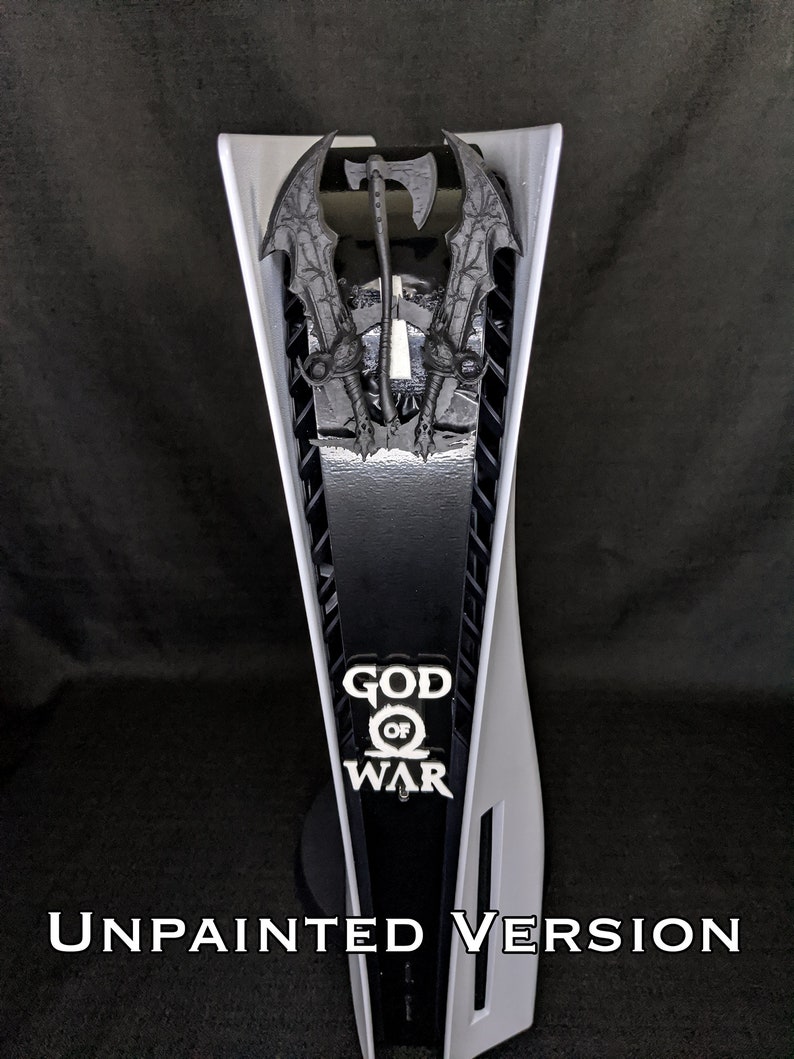 May include: A white and black PlayStation 5 console with a decorative panel featuring the "God of War" logo and weapon designs. The text "UNPAINTED VERSION" is displayed at the bottom.