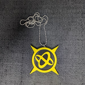 May include: A yellow and black pendant necklace with a silver chain. The pendant has a circular design with a yellow border and four pointed edges. Inside the border is a black circle with a yellow intertwined design.