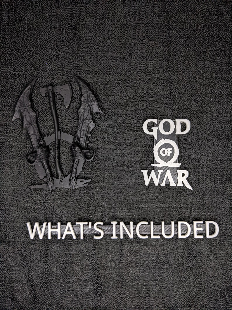 May include: Black 3D-printed decorative set featuring a stylized axe and swords, the words "GOD OF WAR", and the phrase "WHAT'S INCLUDED" in white. The items are arranged on a textured black surface.