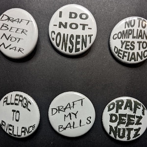 May include: Six white round buttons with black text. The buttons have various phrases, including "Draft Beer Not War," "I Do Not Consent," and "No to Compliance Yes to Defiance." Other buttons say "Allergic to Surveillance," "Draft My Balls," and "Draft Deez Nutz."