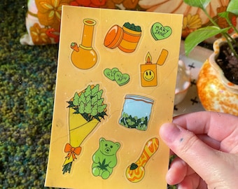 May include: A sheet of stickers with a yellow background featuring various cannabis-themed designs, including a bong, a bag of weed, a gummy bear, a lighter, and a heart with the text "Mary Jane".