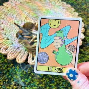 May include: A sticker with a cartoon illustration of a green bong with a blue swirl of smoke. The sticker has the text "THE BONG" at the bottom.
