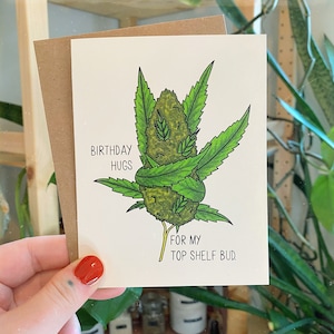 May include: A greeting card with a green marijuana bud illustration. The card reads "Birthday Hugs for my Top Shelf Bud."
