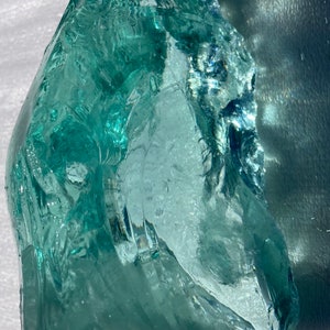 May include: A large, translucent, light green piece of sea glass with a smooth, rounded surface and a few small air bubbles.
