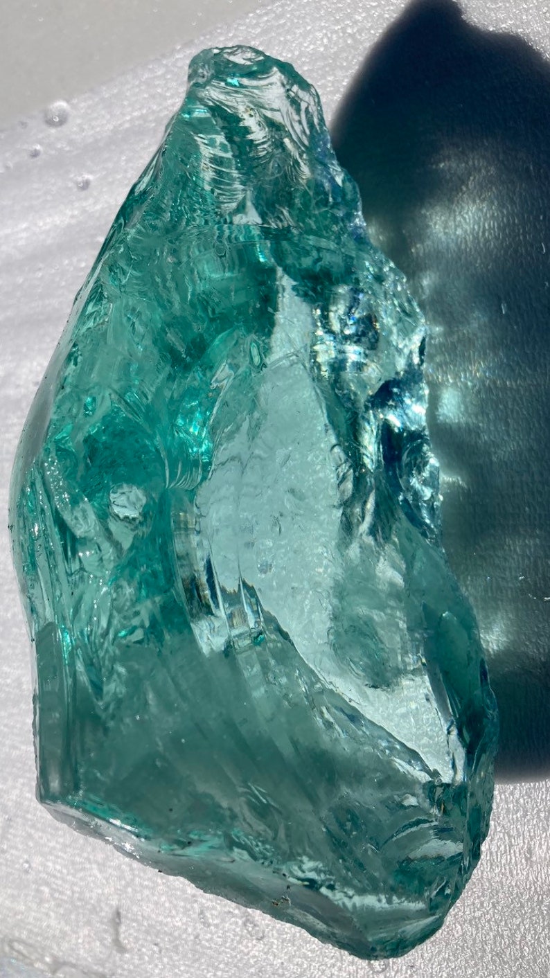 May include: A large, translucent, light green piece of sea glass with a smooth, rounded surface and a few small air bubbles.