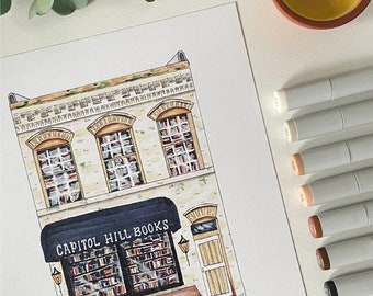 May include: An illustration of Capitol Hill Books, a bookstore with a black awning and the store name in white. The building is beige with three arched windows filled with books. A brown bench sits below the awning. The artwork is on white paper.