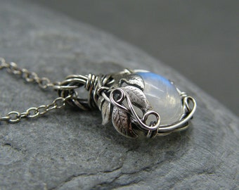 May include: A silver necklace with a moonstone pendant surrounded by silver leaves. The pendant is wire wrapped and has a delicate, nature-inspired design.