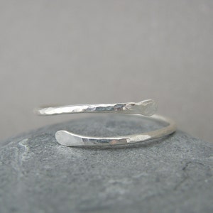 May include: A silver hammered wrap ring with a simple design. The ring is made of a single piece of wire that is wrapped around the finger.