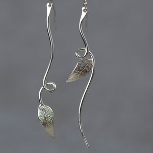 May include: A pair of silver dangle earrings with leaf designs. The earrings are made of thin, twisted wire with a leaf shape at the bottom.