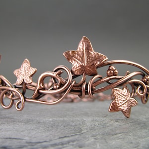 Puede incluir: Un brazalete de alambre de cobre con un delicado diseño de hojas y enredaderas de hiedra. Las hojas son texturizadas y tienen un acabado martillado.