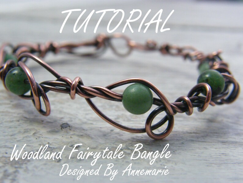 May include: Copper wire wrapped bracelet with green gemstone beads. The bracelet is designed in a vine pattern. The text "Woodland Fairytale Bangle Designed By Annemarie" is below the bracelet.