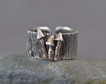 May include: A silver ring with a textured band and three mushroom designs. The mushrooms are made of silver and have a slightly raised appearance.