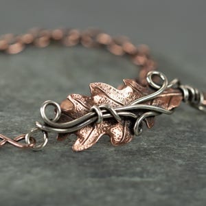 Könnte beinhalten: Ein Armband aus Kupfer und Silber mit einem detaillierten Blattdesign. Das Blatt ist strukturiert und hat ein filigranes Drahtdesign.