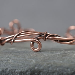 May include: A copper wire bracelet featuring a delicate, interwoven design. The bracelet is crafted from multiple strands of wire that are twisted and turned to create a unique and intricate pattern.