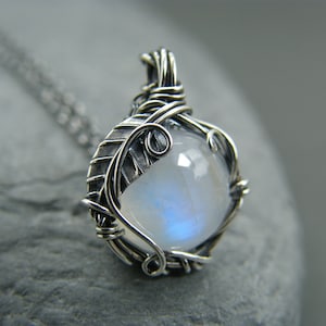 May include: A silver wire wrapped pendant featuring a round moonstone cabochon. The wire is twisted into a leaf design.