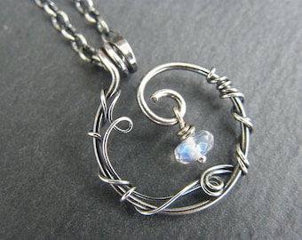 May include: A silver necklace with a delicate wire-wrapped pendant featuring a moonstone gemstone. The pendant is shaped like a circle with a swirl design.
