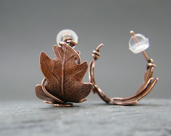 May include: A pair of copper leaf hoop earrings with a textured finish. The earrings are made of wire and have a simple, elegant design.