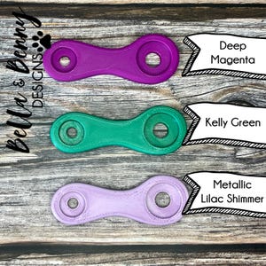 May include: Three 3D-printed chain link connectors in Deep Magenta, Kelly Green, and Metallic Lilac Shimmer. Each connector has two circular ends connected by a curved bar. The Bella & Benny Designs logo is in the upper left corner.
