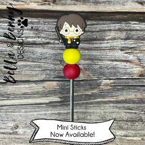 May include: A Harry Potter themed mini stick with a red, yellow, and yellow bead stack and a small figurine of Harry Potter on top. The text "Mini Sticks Now Available!" is on a banner below the stick.