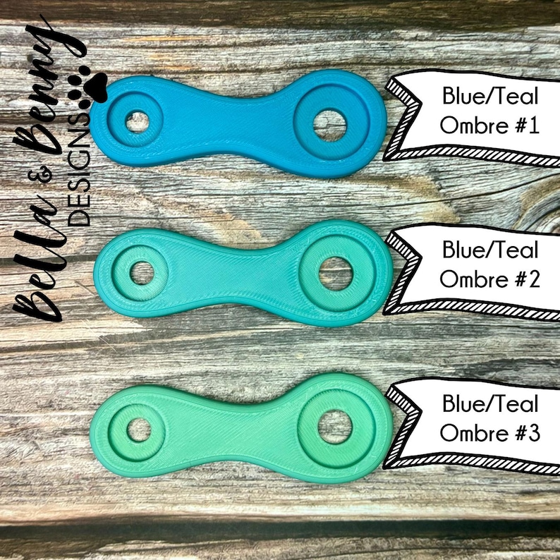 May include: Three blue and teal ombre-colored, dumbbell-shaped objects with circular holes. Each object has a different shade of blue and teal. The text "Blue/Teal Ombre #1", "Blue/Teal Ombre #2", and "Blue/Teal Ombre #3" is displayed.