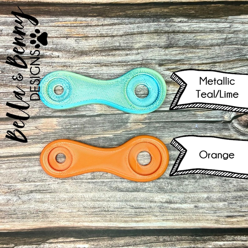 May include: Two 3D-printed, dumbbell-shaped objects. One is teal and lime, the other is orange. Each has two circular holes. Text on the right reads "Metallic Teal/Lime" and "Orange". The Bella & Benny Designs logo is in the upper left.