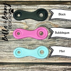 May include: Three colorful, symmetrical, plastic objects in black, bubblegum pink, and mint green. Each has two circular ends connected by a narrow, ridged center. Text labels identify the colors. The Bella & Benny Designs logo is in the upper left corner.