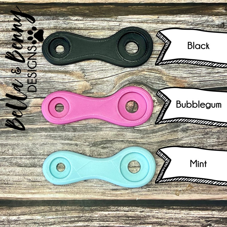 May include: Three colorful, symmetrical, plastic objects in black, bubblegum pink, and mint green. Each has two circular ends connected by a narrow, ridged center. Text labels identify the colors. The Bella & Benny Designs logo is in the upper left corner.